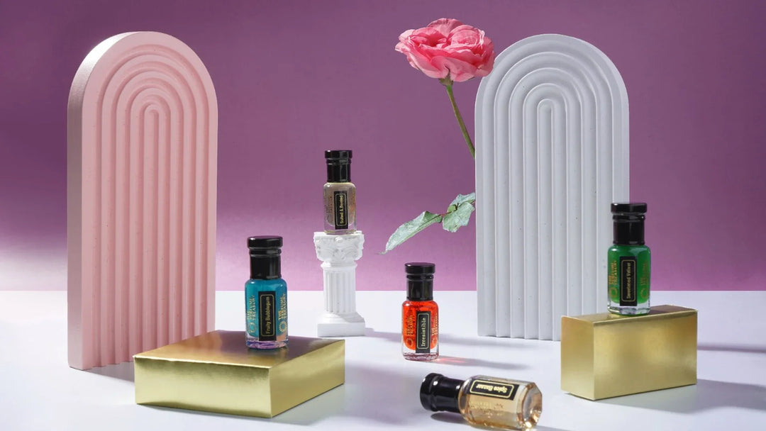 Alcohol free perfume oil bottles in assorted colours by The Perfume Treasury, displayed on gold blocks with pink and white arches and a pink rose