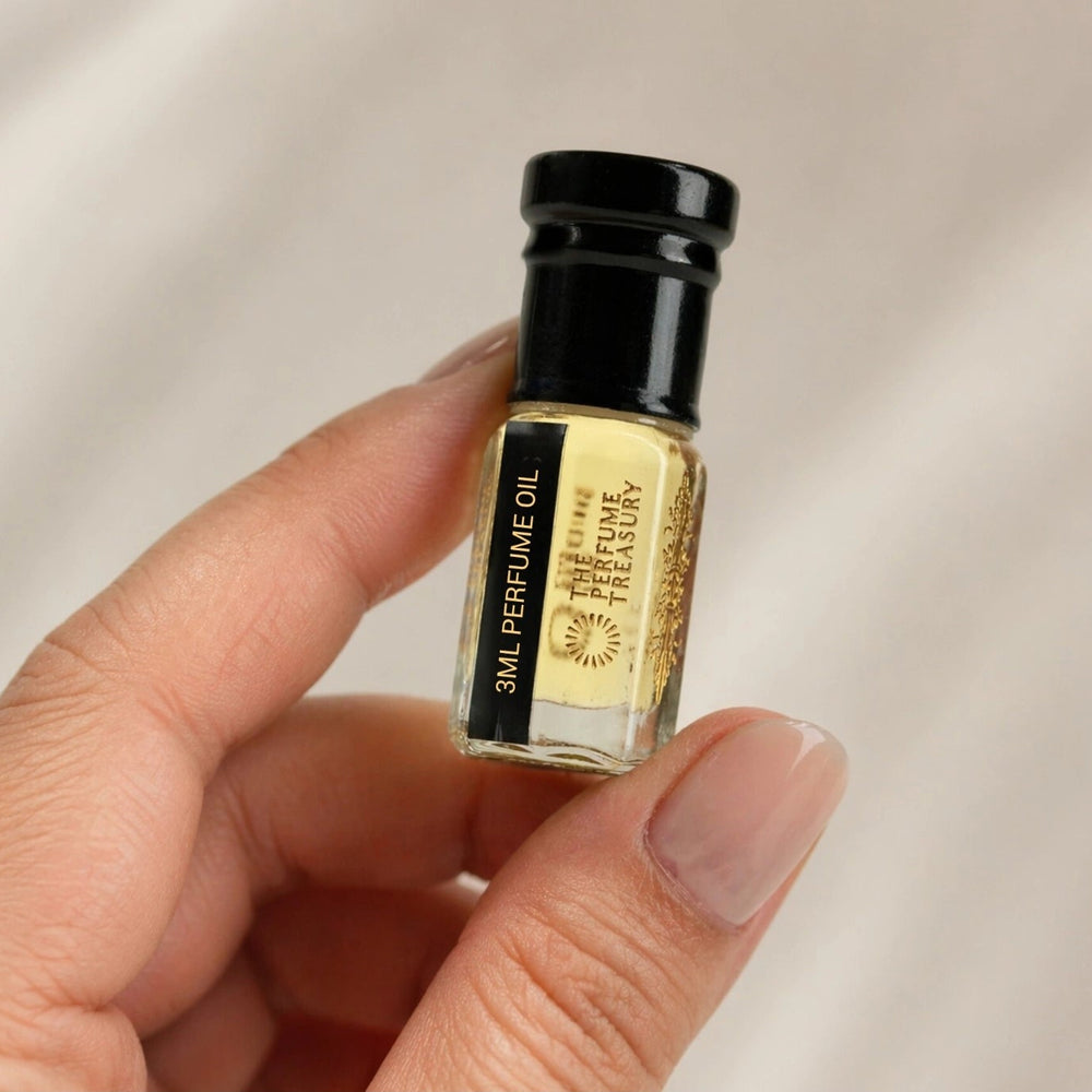 Small clear glass perfume oil bottle with black cap, Nocturnal Woods 3ml attar perfume oil by The Perfume Treasury, golden fragrance oil held between fingers for size reference on neutral background.