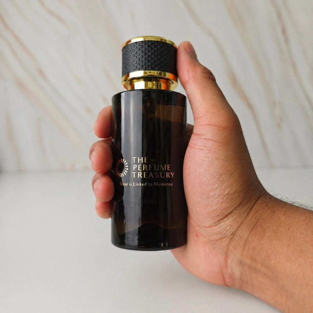 Dark Amber glass parfum spray bottle with black and gold cap, 50ml parfum spray by The Perfume Treasury, held in hand for size reference on neutral background.