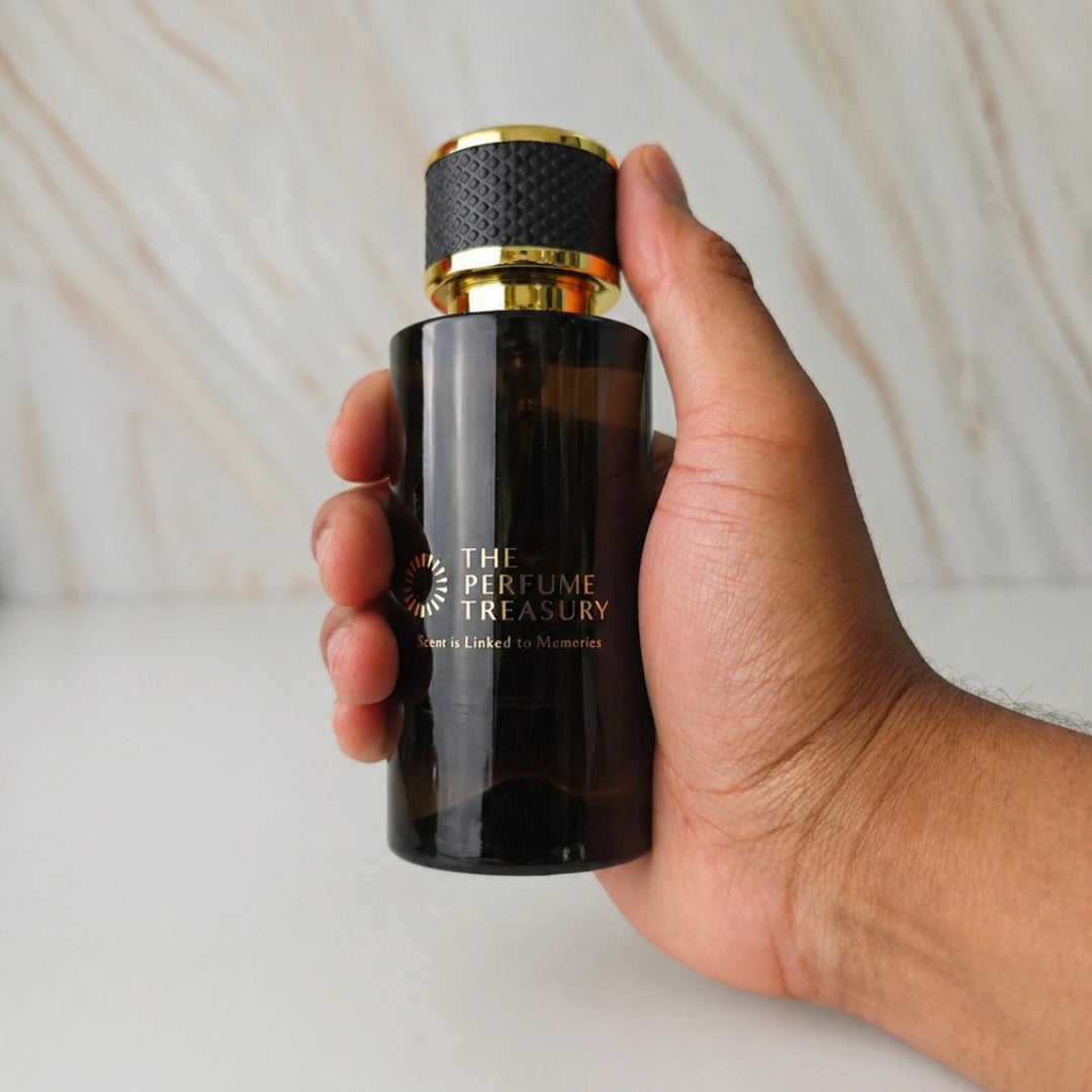 Dark Amber glass parfum spray bottle with black and gold cap, 50ml parfum spray by The Perfume Treasury, held in hand for size reference on neutral background.
