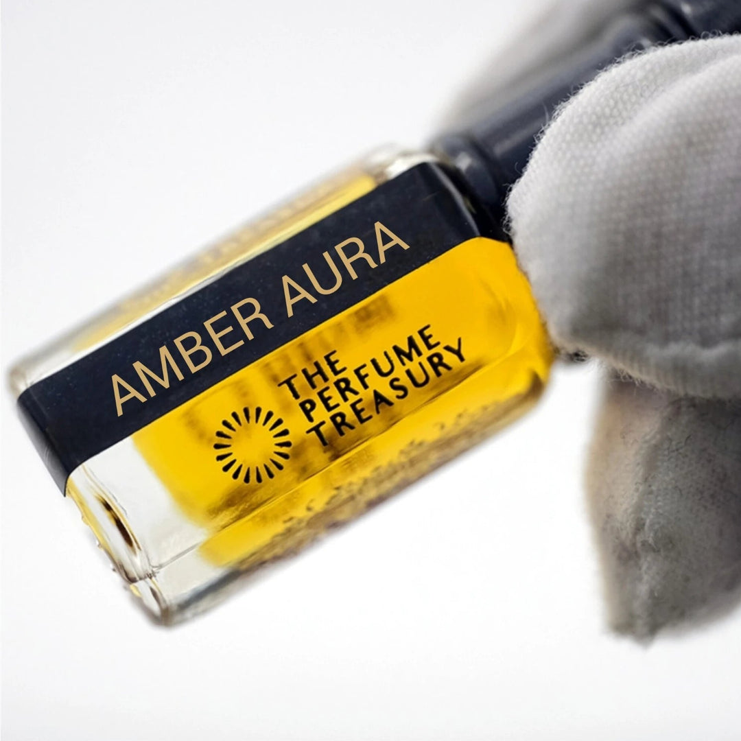 Macro close-up of Amber Aura luxury fragrance oil bottle held with white glove, showcasing radiant amber-gold perfume oil, reflective glass details and premium Arabian attar presentation.