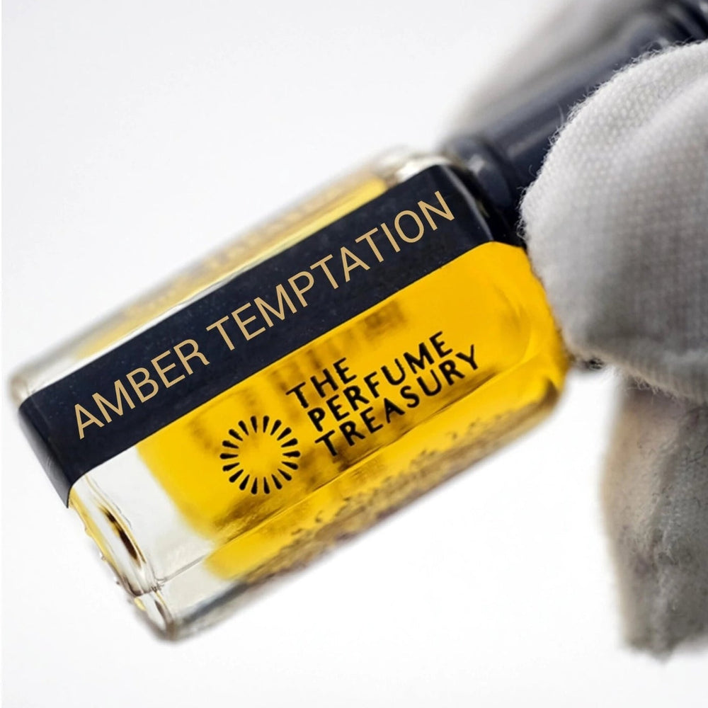 Close-up macro of Amber Temptation fragrance oil bottle held with white glove, showing rich amber-gold oil texture and reflective luxury glass detailing, concentrated Arabian perfume oil in clear glass bottle with black cap.