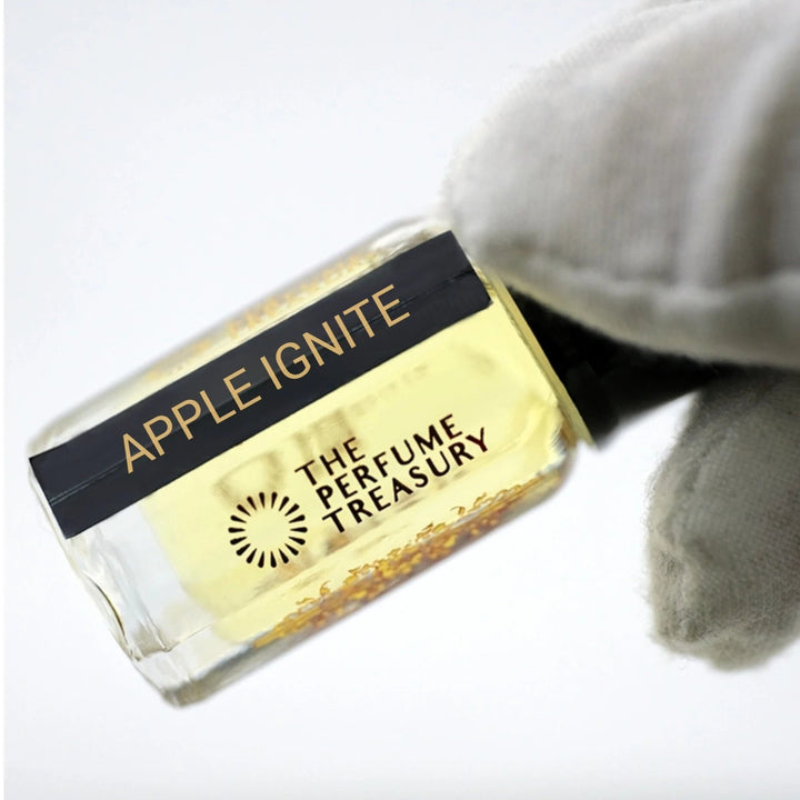 Macro shot of Apple Ignite attar perfume bottle held delicately in a white glove, highlighting pale golden fragrance oil, reflective glass bottle and luxury niche perfume presentation.