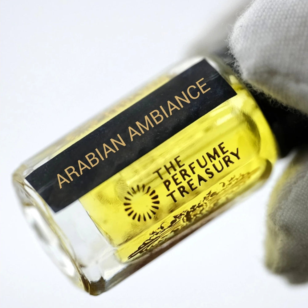 Close-up luxury photograph of Arabian Ambiance attar bottle held with a white glove, showcasing vivid golden perfume oil, clear glass detailing and elegant Arabian fragrance branding.
