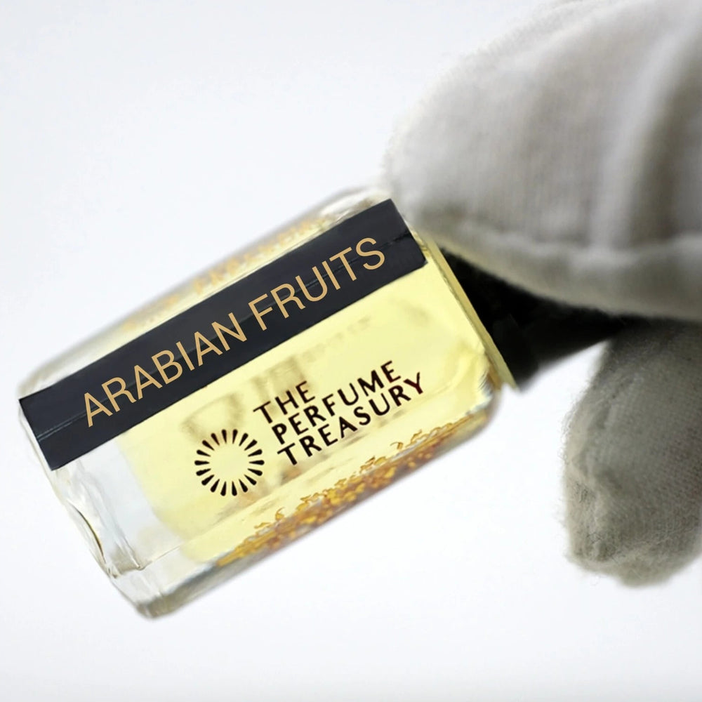 Close-up luxury image of Arabian Fruits attar oil bottle held in white glove, showcasing soft yellow fragrance oil, reflective glass bottle and elegant Arabian perfume styling.