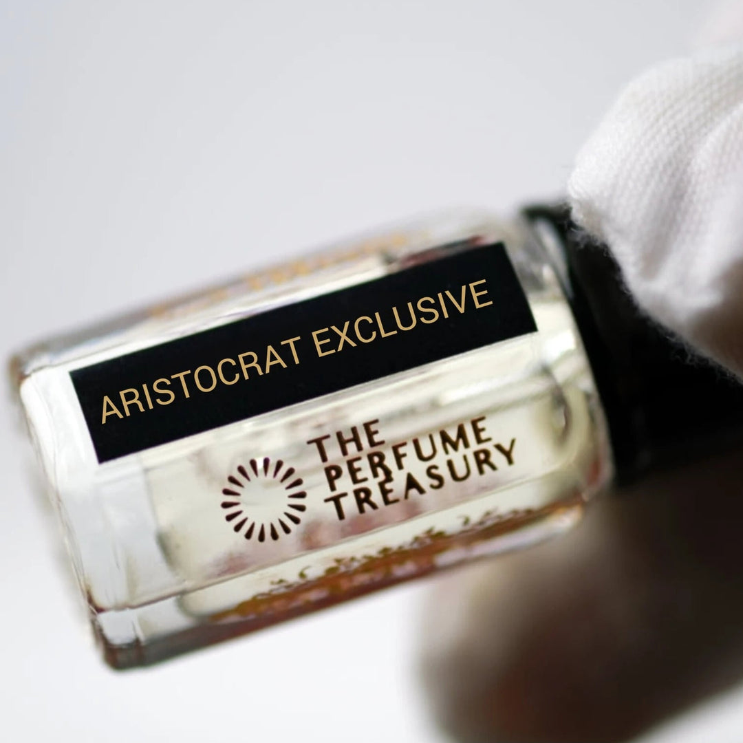 Detailed close-up shot of Aristocrat Exclusive attar perfume bottle held in a white glove, emphasizing clear fragrance oil, reflective glass texture and luxury perfume presentation.