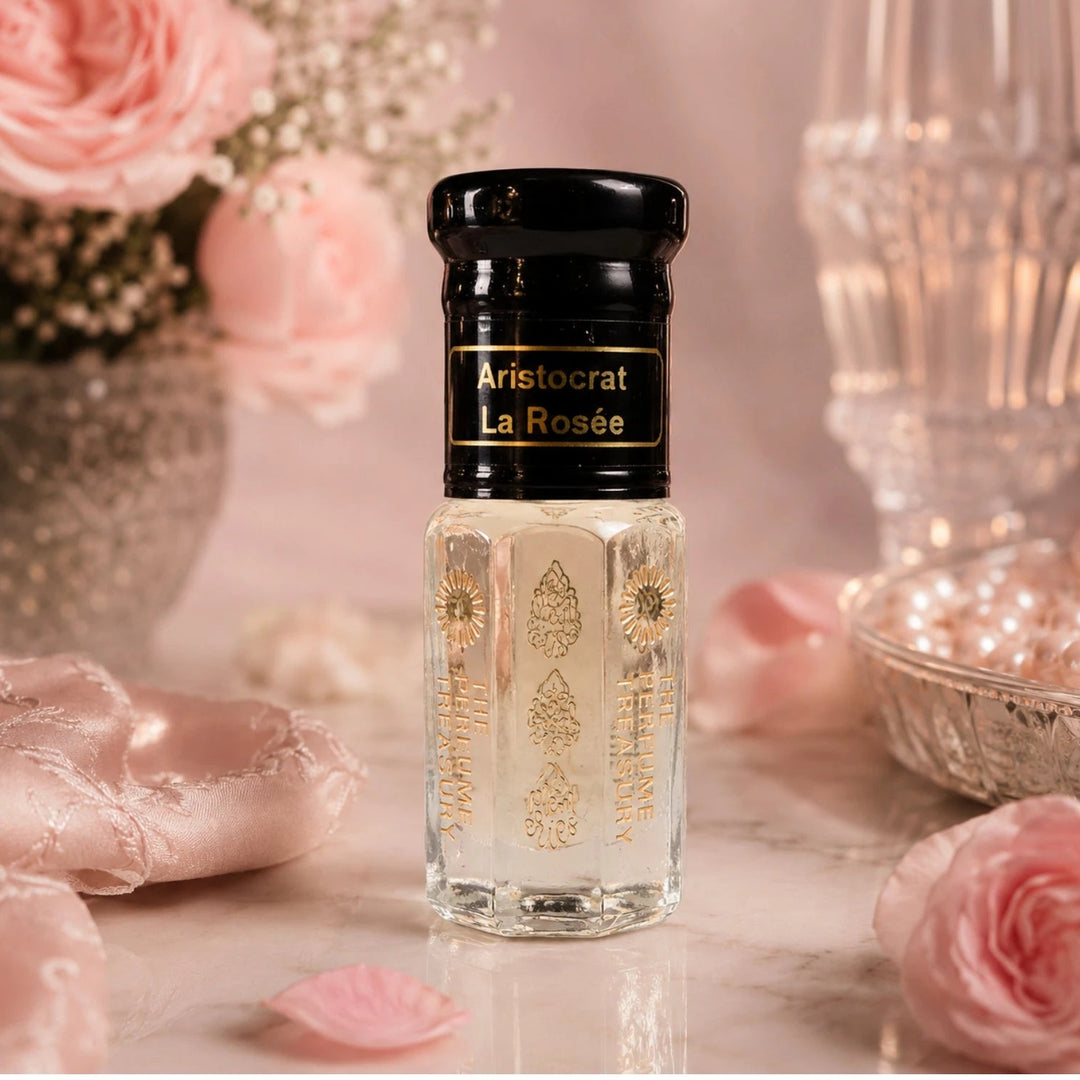 Romantic luxury composition of Aristocrat La Rosée perfume oil surrounded by pink roses, pearls and satin fabric with soft glowing light creating an elegant fragrance ambiance.