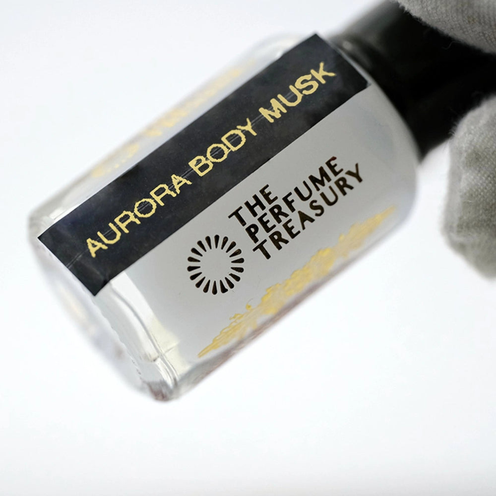 Luxury close-up photograph of Aurora Body Musk attar bottle held in a white glove, highlighting the creamy white fragrance oil, sleek black label and polished glass details.