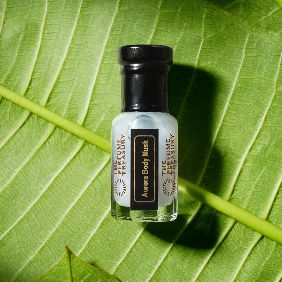 Fresh botanical lifestyle image of Aurora Body Musk perfume oil placed on vibrant green tropical leaves with natural sunlight and soft shadows creating an earthy luxury atmosphere.