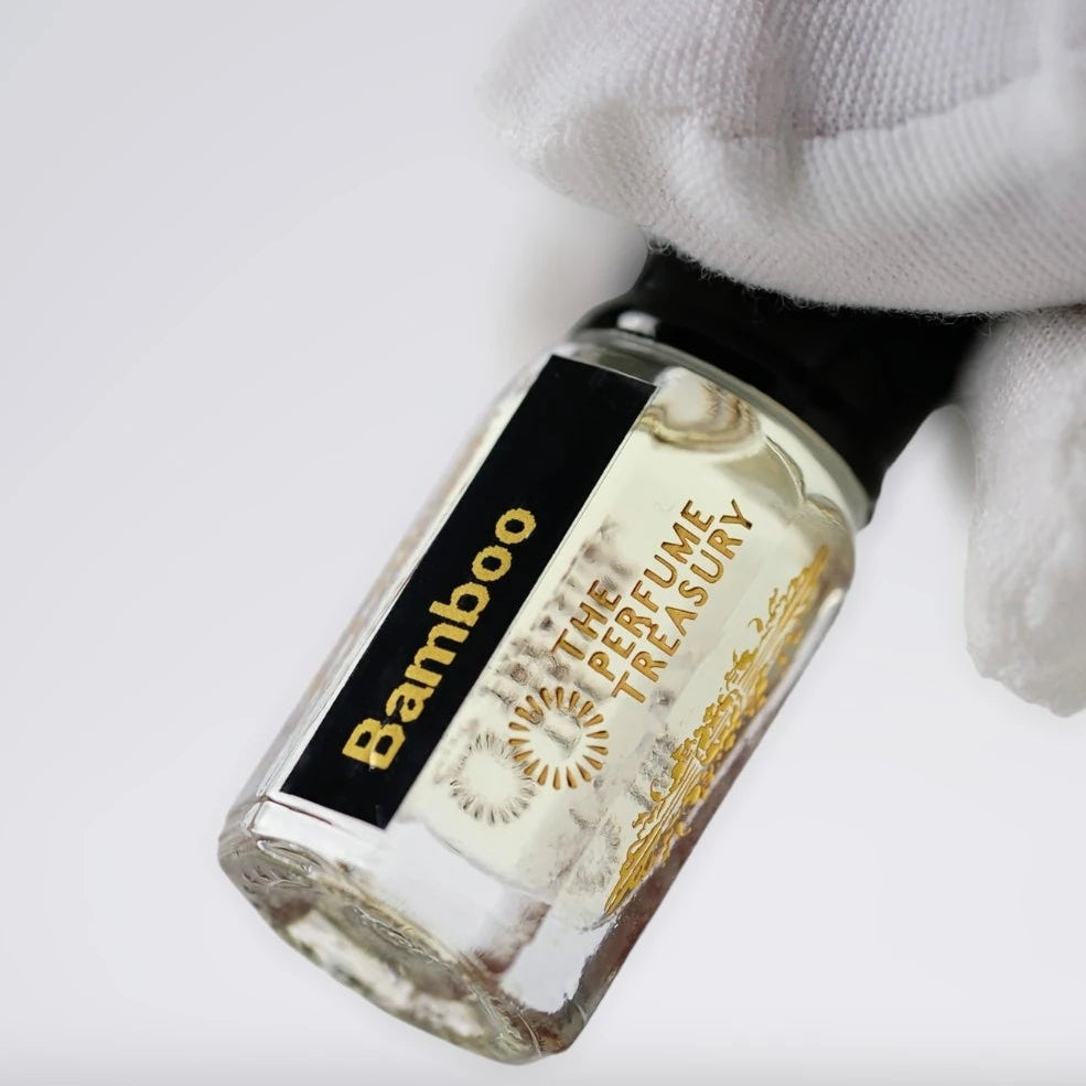 Macro close-up of Bamboo attar perfume bottle delicately held in a white glove, showcasing transparent golden fragrance oil, luxury branding and polished glass bottle texture.