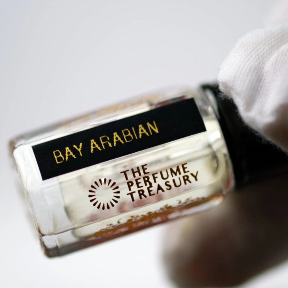 Close-up macro of Bay Arabian 3ml attar perfume oil bottle by The Perfume Treasury, showing clean transparent fragrance oil and reflective glass finish, luxury oil in clear bottle with black cap.