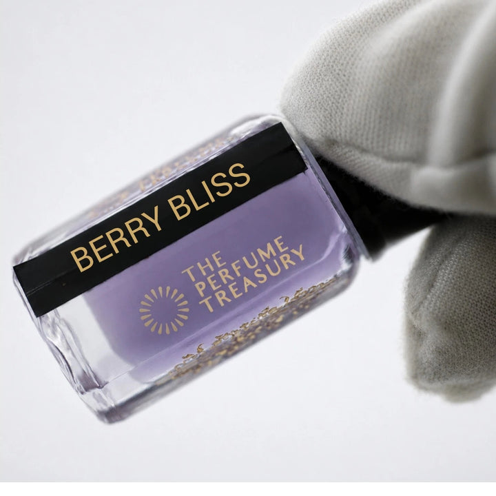 Luxury close-up photograph of Berry Bliss attar perfume bottle held in a white glove, highlighting the lavender-toned fragrance oil, glossy black label and refined glass details.