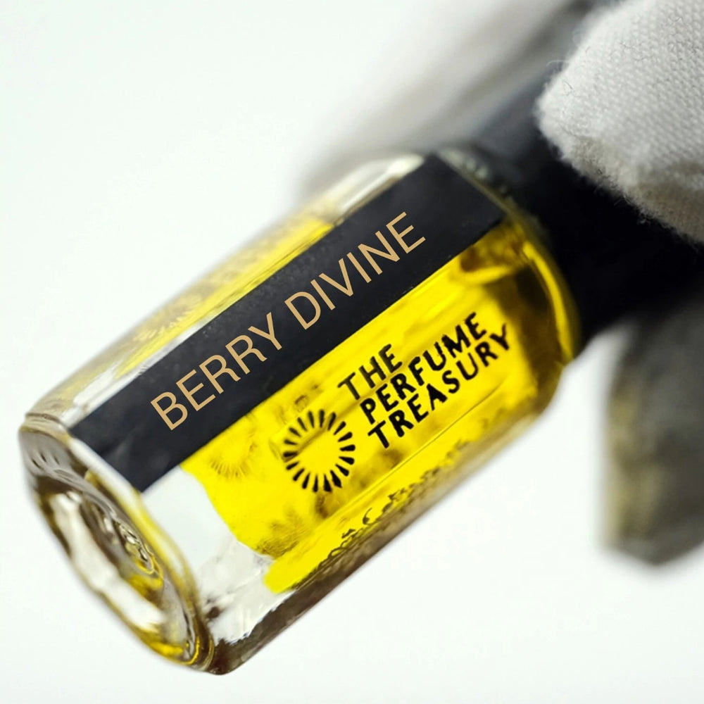 Macro close-up of Berry Divine attar perfume bottle delicately held in a white glove, showcasing vivid golden fragrance oil, elegant branding and crystal-clear glass texture.