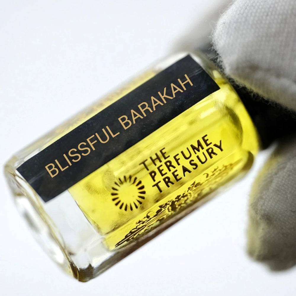 Luxury close-up photograph of Blissful Barakah perfume oil bottle held in a white glove, emphasizing the glossy glass texture, bright fragrance oil and sophisticated branding.