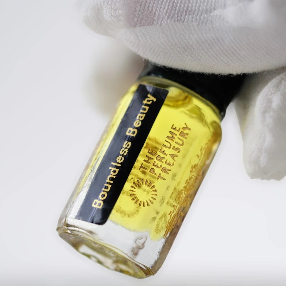Close-up of Boundless Beauty attar perfume oil  bottle held in white glove, showcasing golden fragrance oil in luxury glass vial.