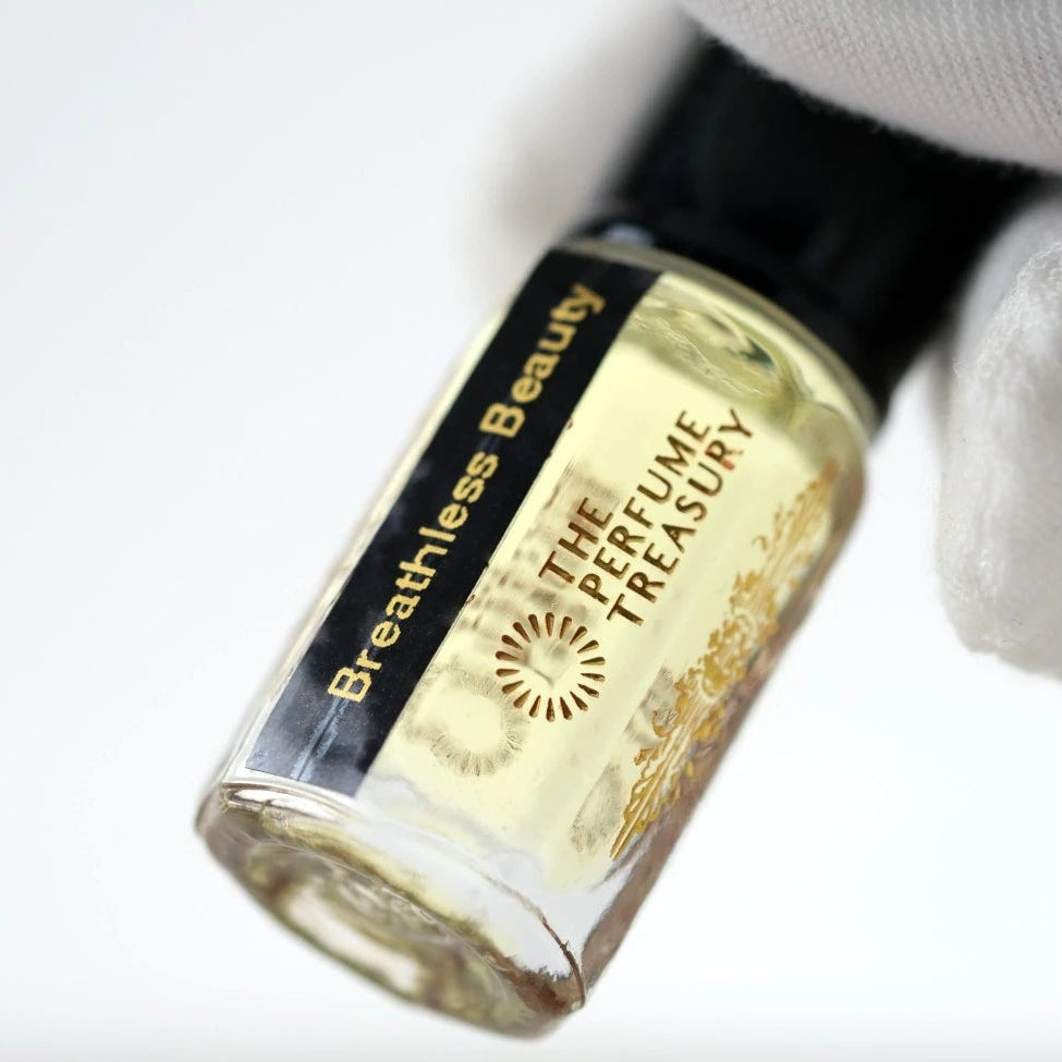 Close-up macro of Breathless Beauty 3ml attar perfume oil bottle held with white glove, showing luminous golden oil texture and reflective glass detail, luxury fragrance oil in clear glass bottle with black cap.