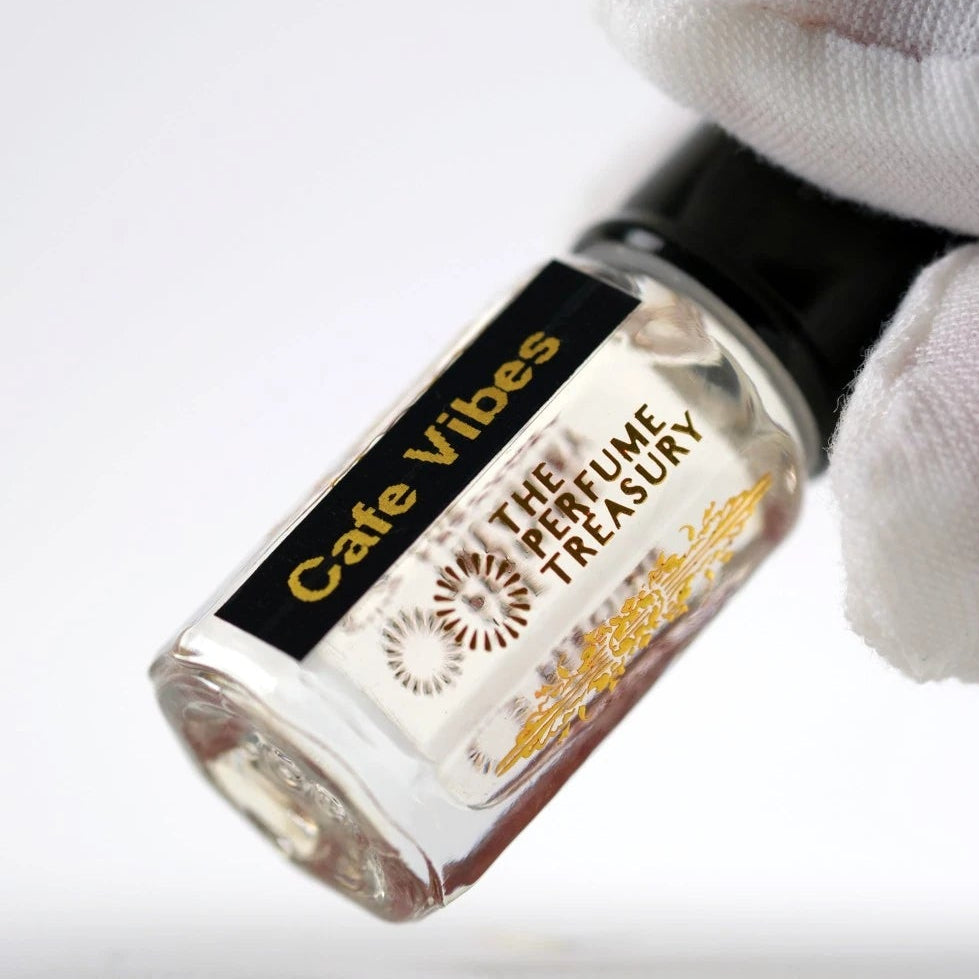 Cafe Vibes perfume oil held in white glove, showcasing artisan fragrance oil presentation in elegant luxury glass bottle.