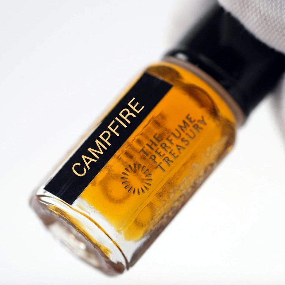 Close-up of Campfire perfume oil bottle held in white glove, highlighting warm amber concentrated fragrance oil by The Perfume Treasury.