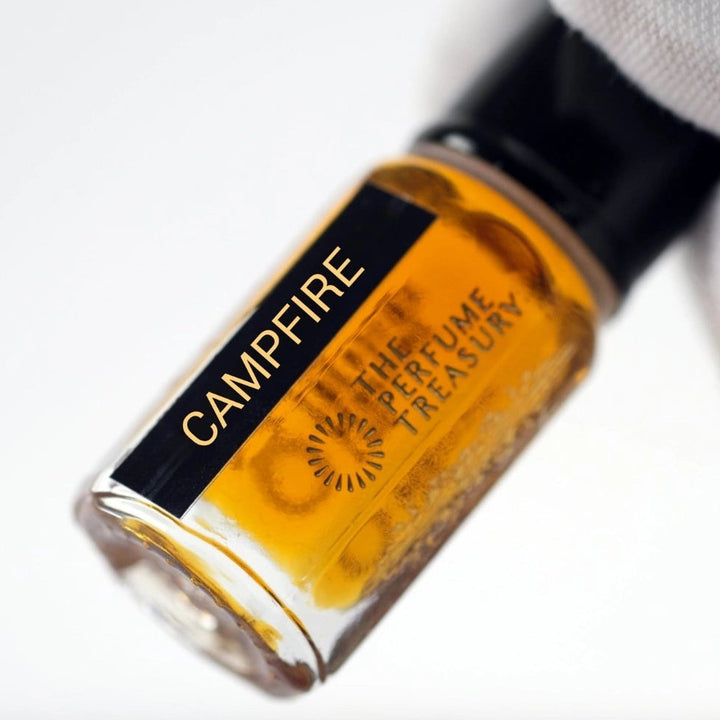 Close-up of Campfire perfume oil bottle held in white glove, highlighting warm amber concentrated fragrance oil by The Perfume Treasury.
