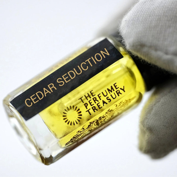 Close-up of Cedar Seduction perfume oil bottle held in white glove, showcasing vibrant woody concentrated fragrance oil.