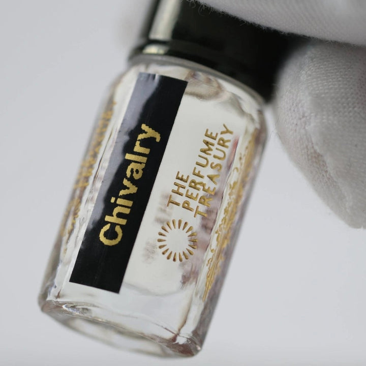 Close-up of Chivalry glass perfume oil bottle held with white glove highlighting luxury fragrance details.