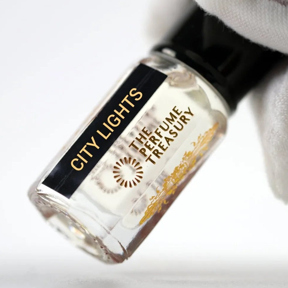 Close-up macro of City Lights 3ml attar perfume oil bottle held with white glove by The Perfume Treasury, showing transparent fragrance oil and reflective glass texture, luxury perfume oil.