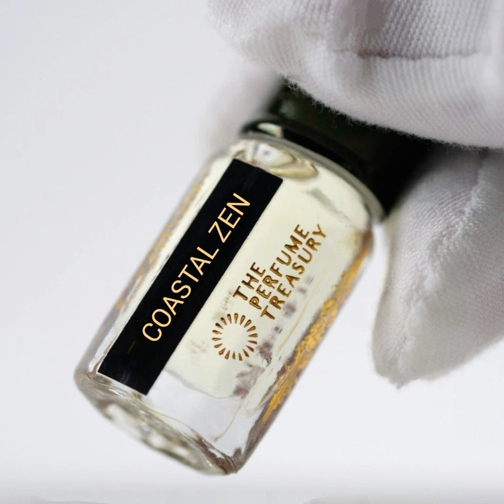 Close-up of Coastal Zen premium perfume oil bottle held with white glove highlighting elegant luxury fragrance craftsmanship and gold accents.