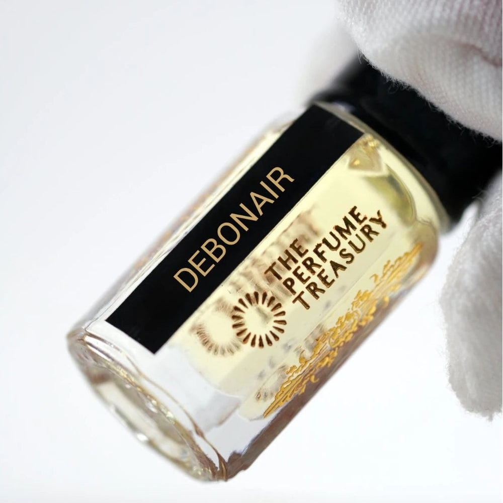 Close-up of Debonair attar perfume oil bottle held with white glove by The Perfume Treasury, showing premium glass detail and pale golden fragrance oil