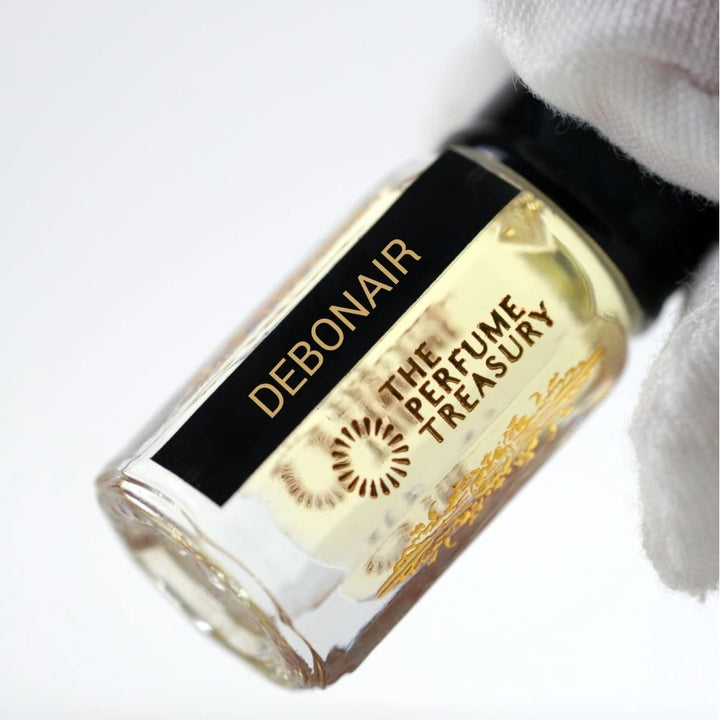 Close-up of Debonair attar perfume oil bottle held with white glove by The Perfume Treasury, showing premium glass detail and pale golden fragrance oil