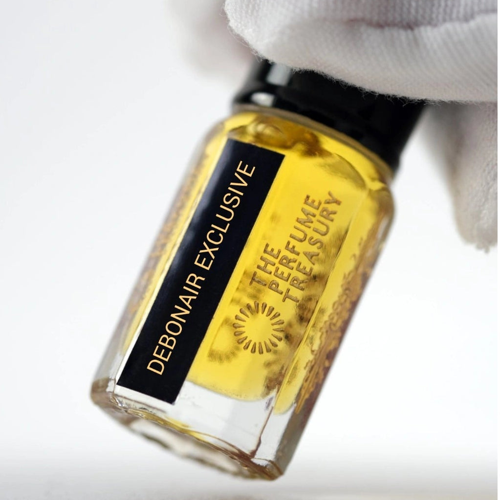 Close-up product photograph of Debonair Exclusive attar perfume oil by The Perfume Treasury held in a white glove with focus on premium branding and golden fragrance oil.