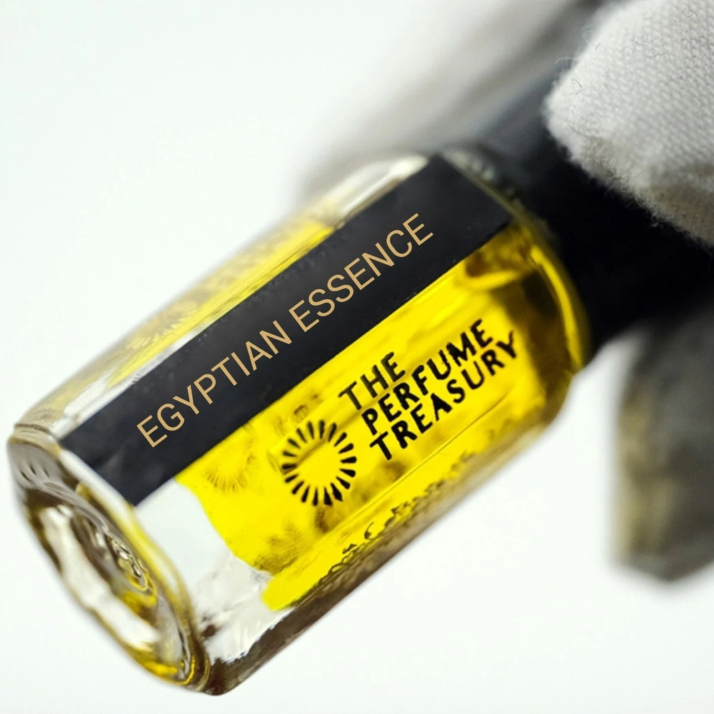 Luxury close-up of Egyptian Essence attar bottle held in a white glove, highlighting the rich golden fragrance oil, glossy glass finish and sophisticated gold-lettered label.