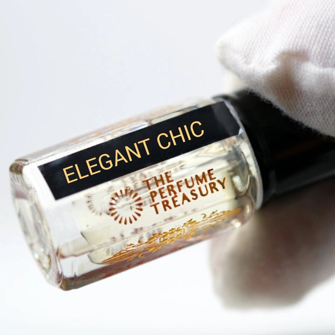 Close-up angled view of Elegant Chic attar perfume oil by The Perfume Treasury held with a white glove, showcasing the premium glass bottle, gold branding and alcohol-free perfume oil presentation.