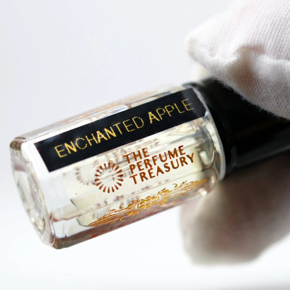 Angled close-up image of Enchanted Apple attar perfume oil by The Perfume Treasury held in a white glove, highlighting the premium bottle design and alcohol-free fragrance oil presentation.