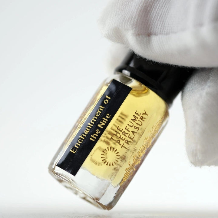 Close-up angled image of Enchantment of the Nile attar perfume oil by The Perfume Treasury held in a white glove, highlighting the luxury bottle design and premium alcohol-free perfume oil presentation.