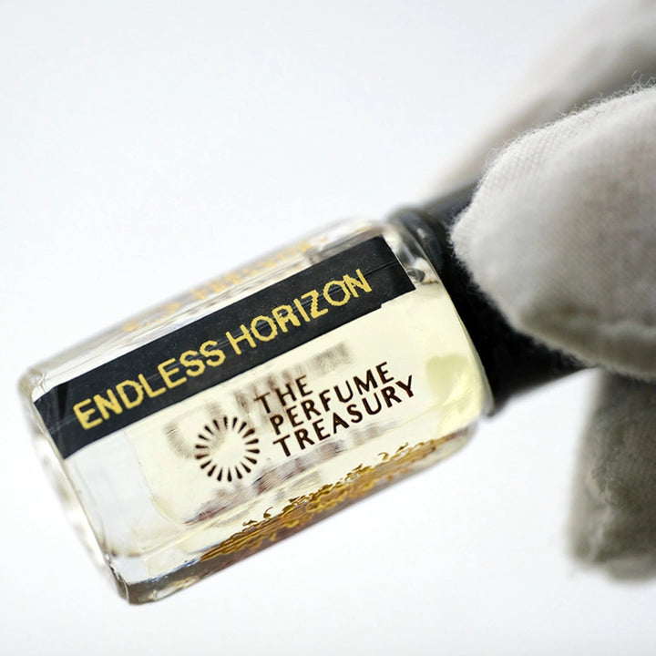 Angled close-up photograph of Endless Horizon attar perfume oil by The Perfume Treasury held in a white glove, showcasing the premium bottle design and luxury alcohol-free fragrance oil presentation.