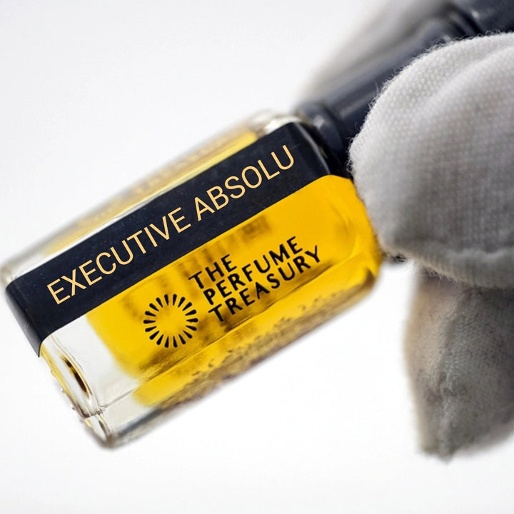 Close-up angled image of Executive Absolu attar perfume oil by The Perfume Treasury held in a white glove, showcasing the clear glass bottle, rich golden fragrance oil and premium presentation.