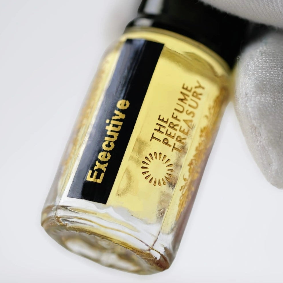 Close-up angled image of Executive attar perfume oil by The Perfume Treasury held in a white glove, showcasing the clear glass bottle, golden fragrance oil and premium presentation.