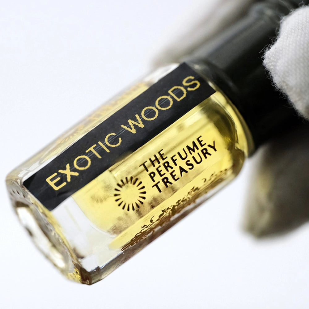 Angled close-up photograph of Exotic Woods attar perfume oil by The Perfume Treasury held in a white glove, showcasing the premium bottle design and luxury alcohol-free fragrance oil presentation.