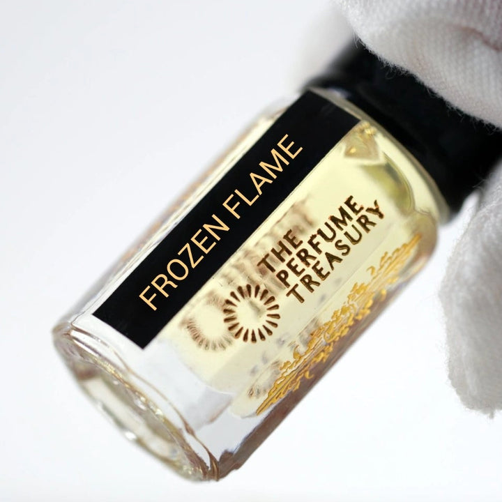 Close-up of Frozen Flame attar perfume oil by The Perfume Treasury, highlighting the pale golden fragrance oil, black label and decorative gold bottle detailing.