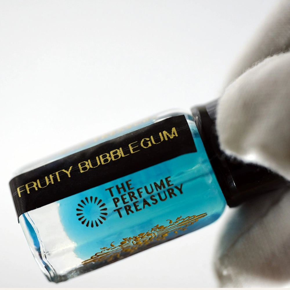 Close-up macro of Fruity Bubblegum attar perfume oil bottle held with white glove by The Perfume Treasury, showing vibrant blue fragrance oil and glossy glass detail.