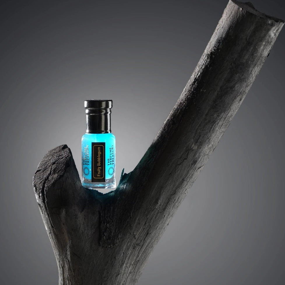 Fruity Bubblegum attar perfume oil by The Perfume Treasury placed on dark wood branch, luxury fragrance oil lifestyle product photography with blue liquid bottle.