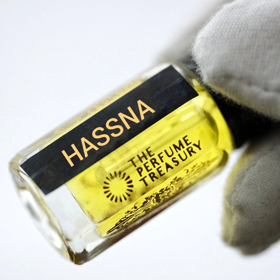Close-up of Hassna Attar Perfume Oil by The Perfume Treasury, 3ml perfume oil bottle with black cap and label held against a soft white background.