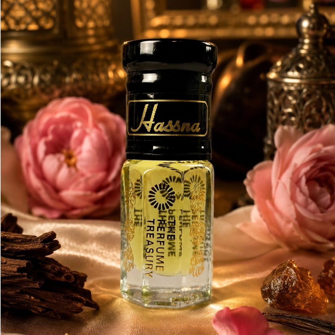 Hassna Attar Perfume Oil by The Perfume Treasury displayed on luxurious satin fabric surrounded by pink roses, vanilla pods and amber resin with warm golden lighting.