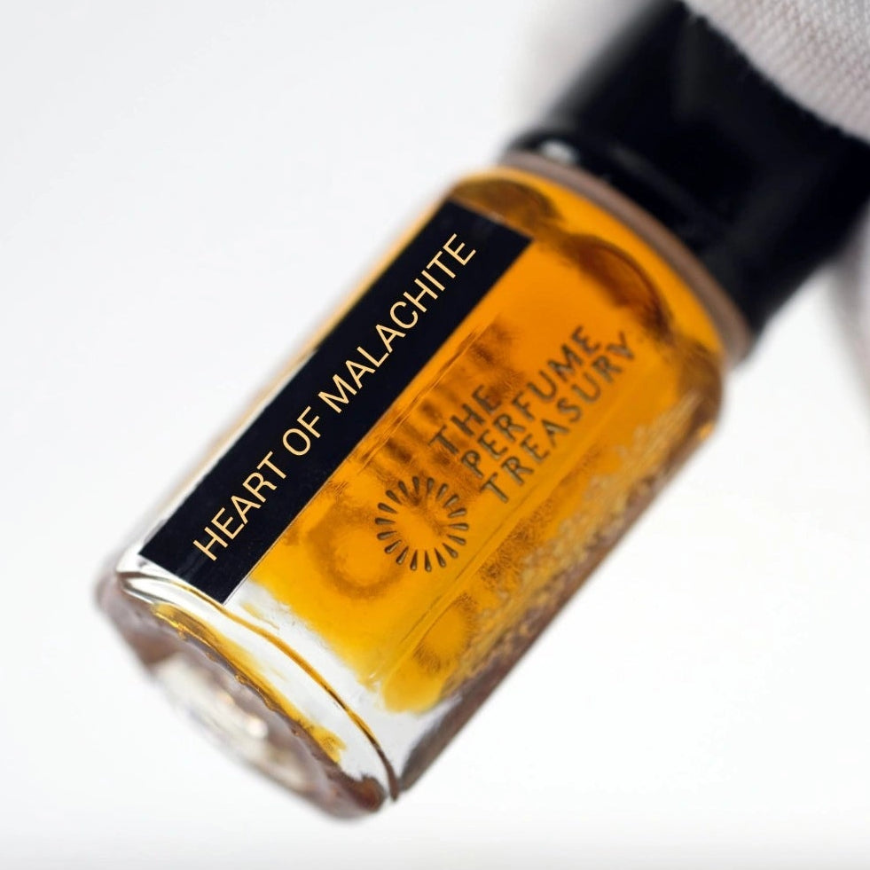 Close-up of Heart of Malachite Attar Perfume Oil by The Perfume Treasury, 3ml perfume oil bottle with black cap and label held against a soft white background.
