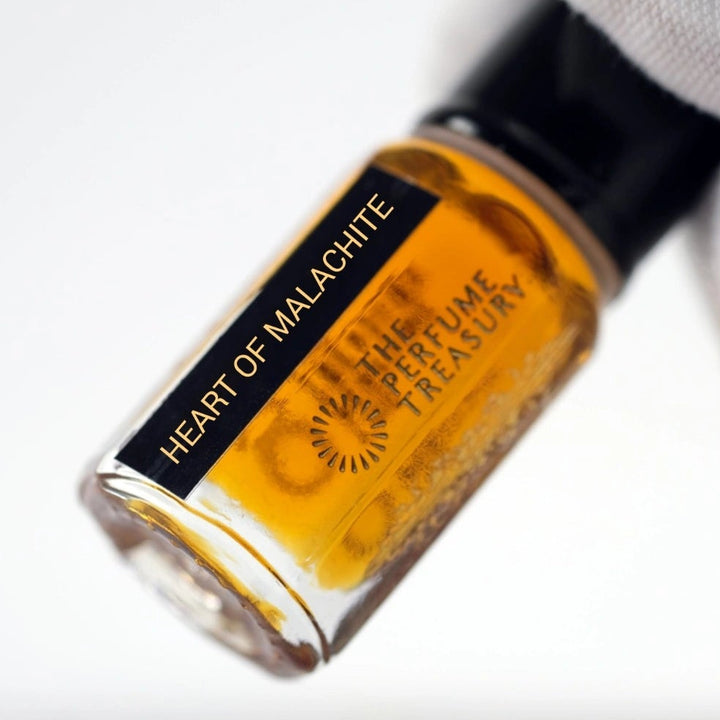 Close-up of Heart of Malachite Attar Perfume Oil by The Perfume Treasury, 3ml perfume oil bottle with black cap and label held against a soft white background.