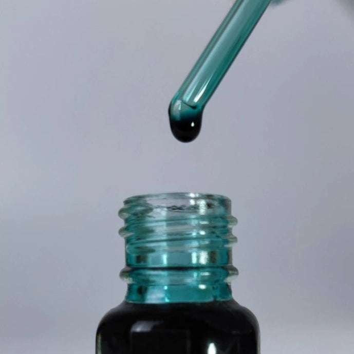 Glass applicator with a drop of Imperial Blue Attar Perfume Oil above the open 3ml bottle by The Perfume Treasury, highlighting the precision oil applicator and luxury fragrance presentation.