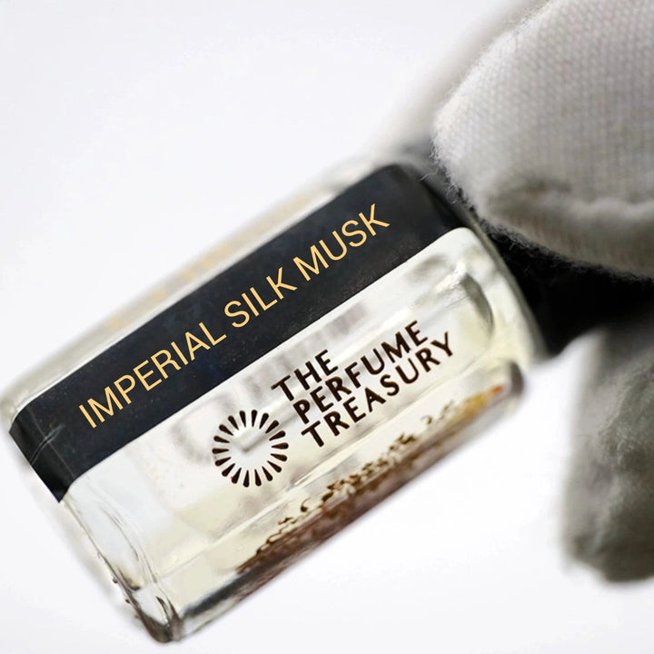 Close-up of Imperial Silk Musk Attar Perfume Oil by The Perfume Treasury, 3ml perfume oil bottle with black cap and label held against a soft white background.