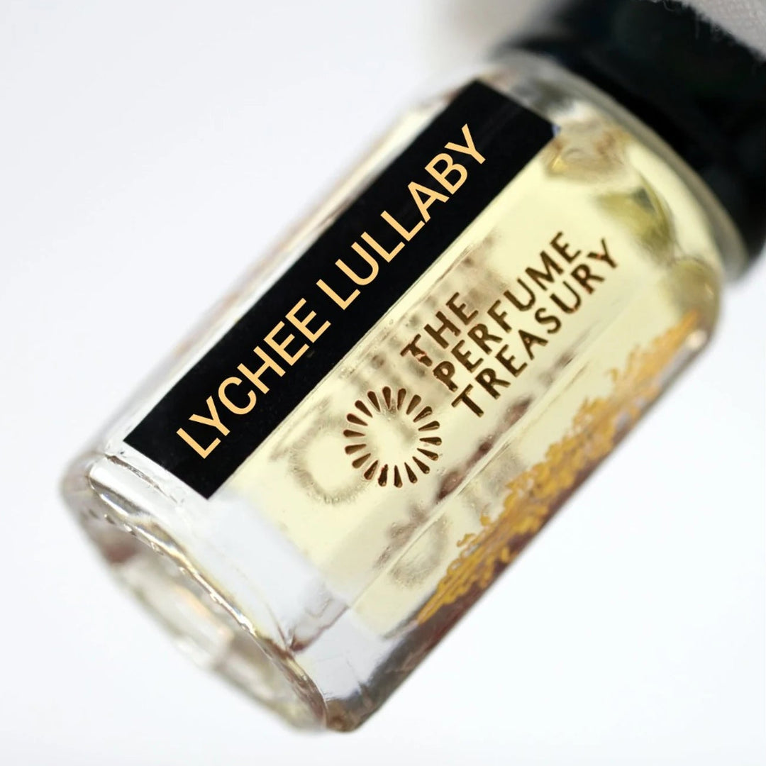 A close-up angled shot of a small clear glass perfume oil bottle containing pale yellow liquid, with a black label reading &