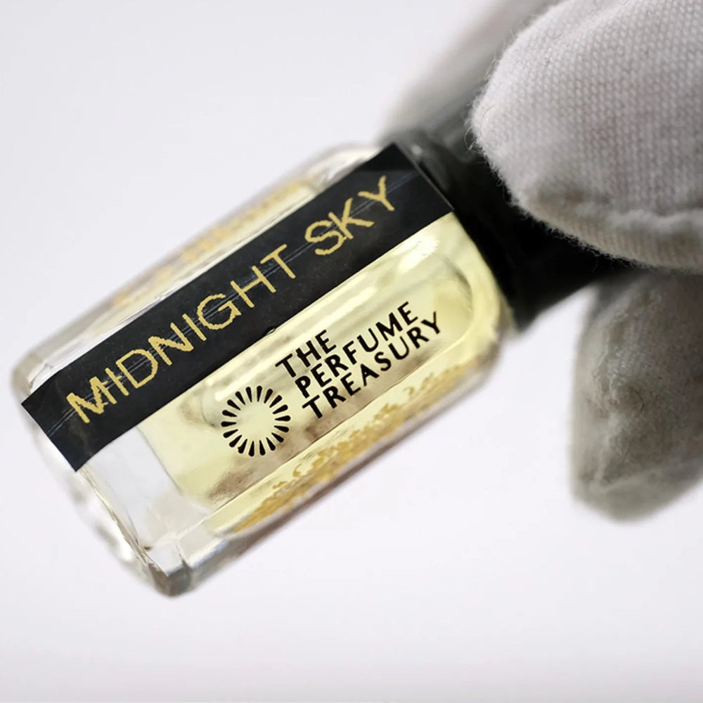 Close-up macro of Midnight Sky 3ml attar perfume oil bottle held with white glove by The Perfume Treasury, showing clear fragrance oil and reflective glass texture, luxury perfume oil.