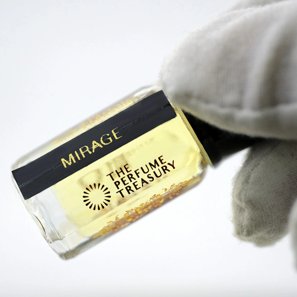 Close-up macro of Mirage 3ml attar perfume oil bottle by The Perfume Treasury, showing pale golden translucent fragrance oil and fine glass detail, luxury oil in clear bottle with black cap.